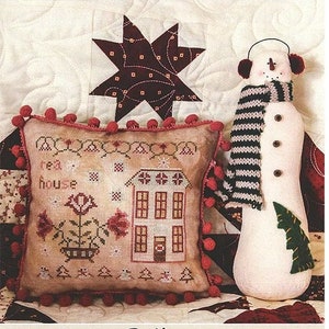 Può includere: Modello di punto croce per una casa da tè con tetto rosso e pareti bianche. Il modello fa parte della serie "Case su Peppermint Lane", progettata da Lori Pengelly. Il modello è mostrato su un cuscino con pompon rossi attorno al bordo.