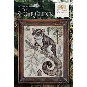 May include: Framed cross-stitch art featuring a sugar glider perched on a branch. The artwork includes text that reads "A Year in the Woods II #2 The Sugar Glider" and a "Cottage Garden Samplings" logo. The color palette includes browns, greens, and creams.
