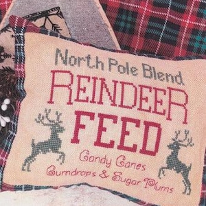 May include: A beige pillow with red and green embroidery that reads "North Pole Blend Reindeer Feed Candy Canes Gumdrops & Sugar Plums".
