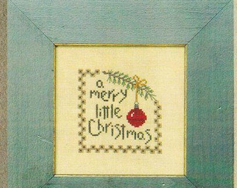 Pode incluir: Uma amostra de ponto de cruz emoldurada com o texto "a merry little Christmas". A amostra apresenta um enfeite vermelho e um raminho verde. A moldura é de cor verde-azulado claro. A parte superior da imagem tem o texto "Bent Creek Classics."