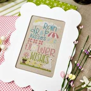 May include: White frame with a scalloped edge, featuring a cross-stitch design with the text "Rain drop kisses and flower wishes".