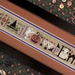 May include: A framed cross-stitch sampler on beige fabric featuring the text It's almost HALLOWEEN. The design includes a black witch hat, a white ghost, an orange jack-o'-lantern, black spiders, bats, a white skeleton, and a black cat.