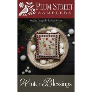 May include: A white fabric sampler featuring a red, green, and brown design of a house, birds, and a tree. The sampler is titled "Winter Blessings" and is part of the Plum Street Samplers collection.