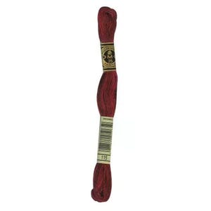 May include: A skein of deep red embroidery floss featuring a gold and black D.M.C. label with the number 25 and a white paper label with a barcode and the number 115. The thread is twisted into a long, slender shape with a textured appearance.