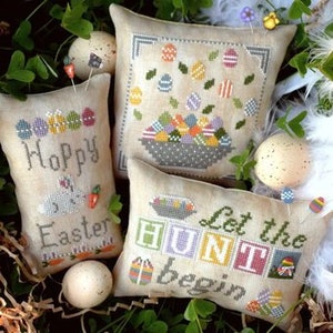 May include: Four embroidered pillow covers with Easter themes. The pillows feature a basket of colorful eggs, a bunny with the text "Happy Easter", a row of eggs with the text "Let the Hunt Begin", and a basket of eggs with a floral design.