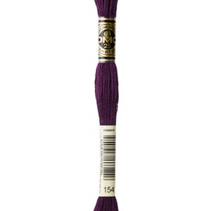 May include: A skein of DMC 25 embroidery floss in a deep purple color, shade 154. The label shows the DMC logo, the thread's length (8 m / 8.7 yd), and a barcode. The floss is tightly wound and ready for use in various needlework projects.
