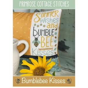 May include: A yellow and green pillow with cross stitch embroidery that reads "Summer Wishes and Bumblebee Kisses". The pillow is sitting on a wooden surface with a sunflower in front of it.