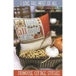 May include: Cross stitch pattern for a pillow featuring a fall-themed design with the text "I Love Fall Most of All". The pillow is in a rustic wooden wagon with fall-colored pumpkins and gourds.
