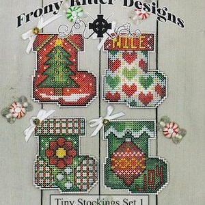 May include: A set of four cross-stitch patterns for tiny Christmas stockings. The patterns include a stocking with a Christmas tree, a stocking with the word "HILE", a stocking with a flower, and a stocking with an ornament and the word "JOY". The patterns are part of a "Mini Series" and are labeled "Tiny Stockings Set 1" and "MNS#11".