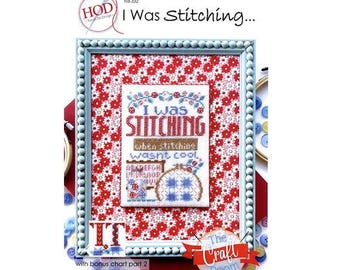 Op de afbeelding: Een ingelijste kruissteeksampler met de tekst "I Was Stitching..." in rood en blauw. De sampler staat tegen een rode bloemenachtergrond en is ingelijst in een lichtblauw, parelversierd frame. Het logo van The Craft Room is zichtbaar.