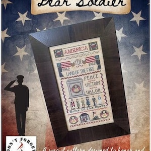 May include: Framed cross-stitch art with a patriotic theme. The artwork features the text "America," "Land of the Free," and "Peace, Victory, Valor." The frame is dark brown, and the background has a flag design with stars.