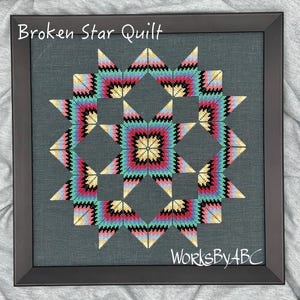 May include: A framed cross-stitch piece depicting a "Broken Star Quilt" design. The quilt is made up of a variety of colors, including pink, blue, green, yellow, and black. The text "WorksByABC" is visible in the bottom right corner of the image.