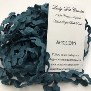 Può includere: Un primo piano di un cordoncino ondulato blu petrolio, un tipo di bordura decorativa in tessuto, con un bordo ondulato e festonato. Il cordoncino è realizzato in 100% cotone e misura 3 yard di lunghezza. L'etichetta riporta "Lady Dot Creates" e "Sequoia".