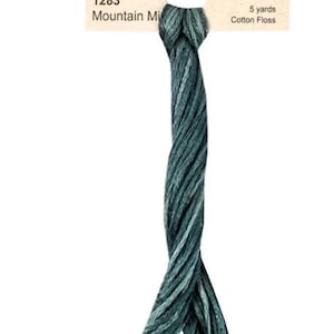May include: A skein of Weeks Dye Works floss in the colour "Mountain Mist" with a label that reads "Weeks Dye Works, Specializing in Hand Over Dyed Fibers, FLOSS COLLECTION, 1283, Mountain Mist, 5 yards, Cotton Floss."