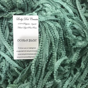 Puede incluir: Primer plano de una pila de ribete de pompon azul verdoso. El ribete está hecho de 100% poliéster y está teñido a mano. El ribete tiene 2 yardas de largo. El texto en la tarjeta dice "Lady Dot Creates", "100% Polyester - 2 yards", "Hand Dyed Pom Poms", "OCALA BLUE", "Follow us on Instagram", "elegantstitch.ladydotcreates", "www.ladydotcreates.com", "ladydotcreates@gmail.com".