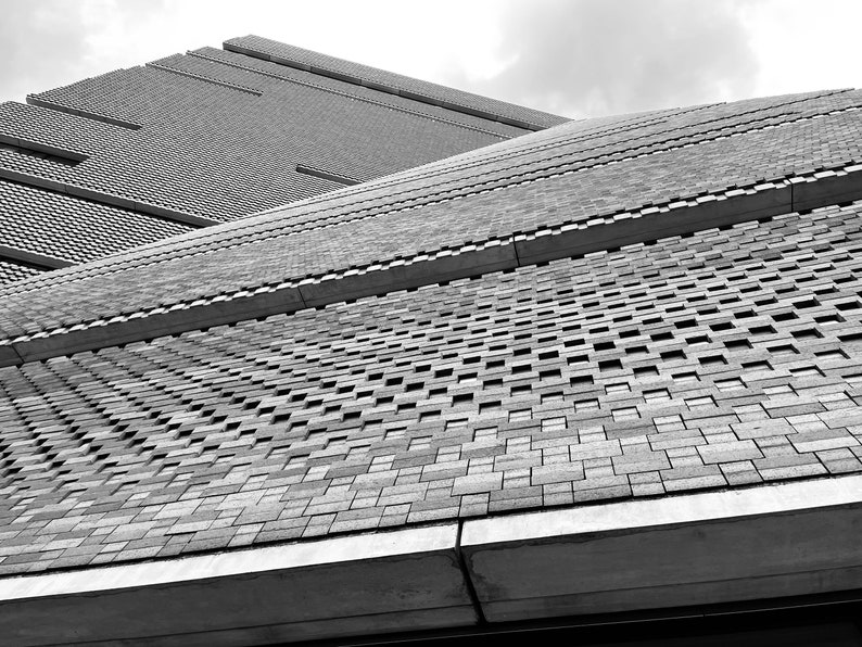 Pu&ograve; includere: Una fotografia in bianco e nero di un edificio con una facciata in mattoni. I mattoni sono disposti in uno schema di quadrati e rettangoli, creando un design geometrico. L'edificio sembra essere molto alto e la foto &egrave; stata scattata da un angolo basso, dando l'impressione di guardare l'edificio dal basso verso l'alto.