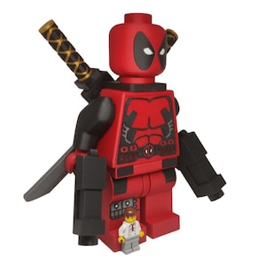 Peut inclure: Une figurine en plastique rouge et noire avec un masque, des taches oculaires noires et un torse imprimé représentant une ceinture et des muscles pectoraux. Le personnage porte deux épées dans le dos et tient deux blasters noirs, avec une minuscule figurine à ses pieds.
