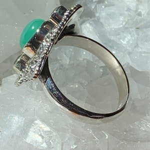 May include: A silver ring with a green gemstone set in a decorative design. The ring is on a white background.