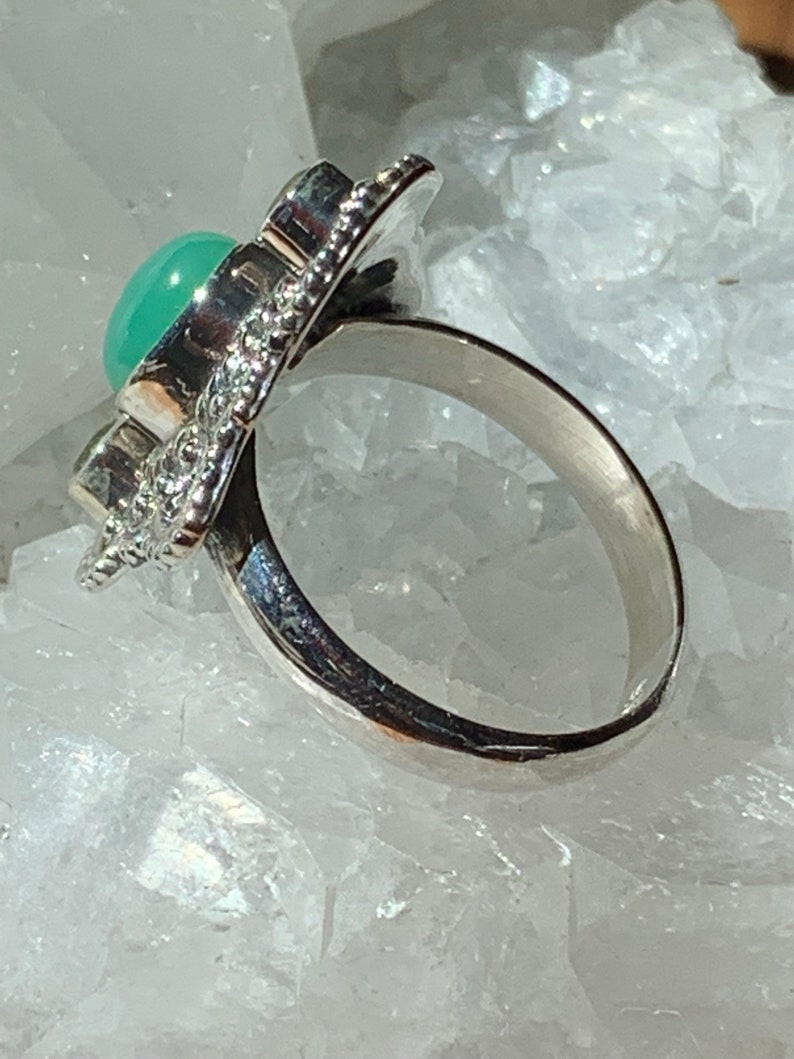 May include: A silver ring with a green gemstone set in a decorative design. The ring is on a white background.