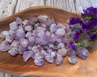 May include: A bowl filled with a large quantity of small, raw amethyst crystals. The crystals are a light purple color and have a variety of shapes and sizes.