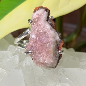 K&ouml;nnte beinhalten: Ein silberner Ring mit einem rosafarbenen und orangefarbenen Kristall in der Mitte. Der Kristall ist ein Cluster aus kleinen Kristallen.