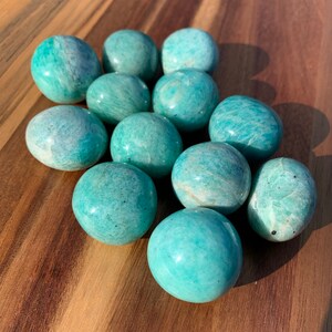 May include: A group of 11 smooth, green, polished amazonite spheres. The spheres are arranged in a pyramid shape on a wooden surface.