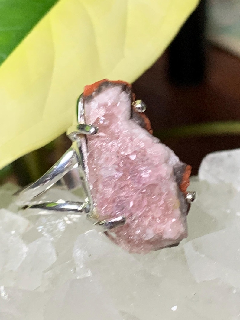 K&ouml;nnte beinhalten: Ein silberner Ring mit einem rosafarbenen und roten Kristall in der Mitte. Der Kristall ist rau und hat eine nat&uuml;rliche, organische Form.
