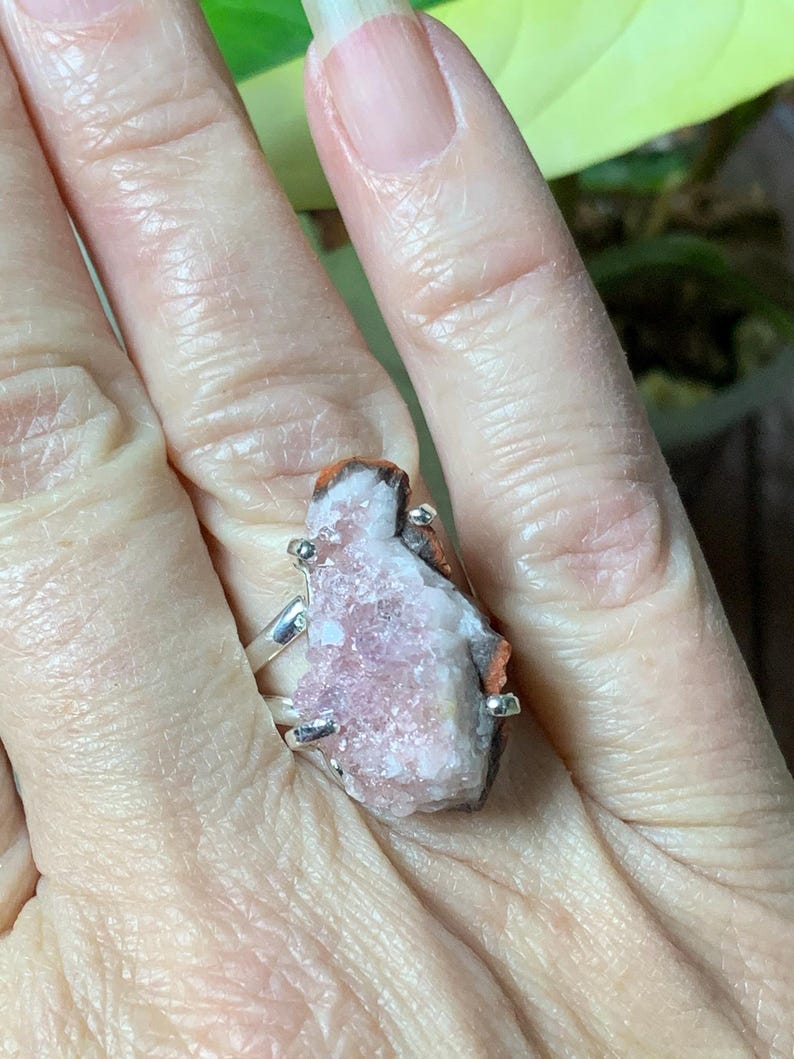 K&ouml;nnte beinhalten: Ein silberner Ring mit einem rosafarbenen und wei&szlig;en Kristallstein. Der Stein ist ein Cluster aus kleinen Kristallen mit einer rauen, nat&uuml;rlichen Textur.