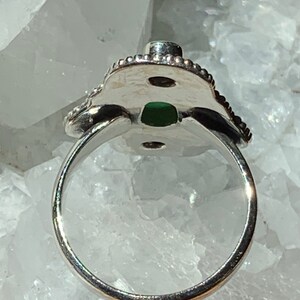 May include: A silver ring with a green stone set in a decorative, ornate design. The ring is open on the back, allowing for easy adjustment.
