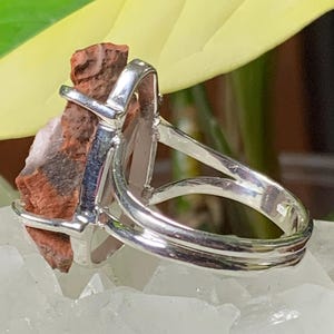 K&ouml;nnte beinhalten: Ein silberner Ring mit einem roten und braunen Stein in der Mitte. Der Ring ist doppelt gefasst und hat eine polierte Oberfl&auml;che.
