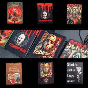 May include: A selection of air fresheners with horror film designs. The designs include "Michael Myers", "Terrifier", "Scream", and "Friday the 13th". Some have text like "Handbook for the Recently Deceased" and "Black is such a happy colour".