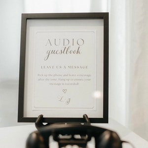 May include: A black framed sign with the text "AUDIO guestbook" and instructions to leave a message after the tone. A black rotary phone sits in front of the sign.