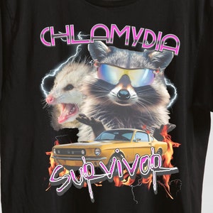 May include: Black t-shirt with a graphic of a raccoon and opossum wearing sunglasses and a yellow car with flames. The text "Chlamydia Survivor" is printed in pink.