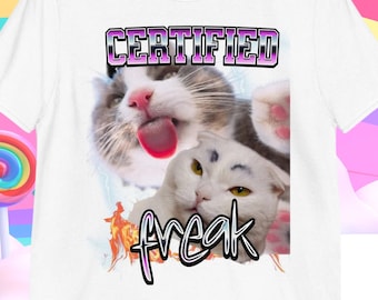 May include: White t-shirt with a graphic of two cats. The text "CERTIFIED freak" is printed in pink and purple letters on the shirt.
