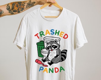 May include: White t-shirt with a colorful graphic of a raccoon sitting next to a trash can and a spilled bottle. The text "Trashed Panda" is above and below the raccoon in rainbow colors.