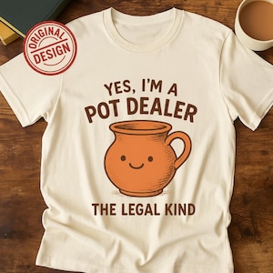 May include: Cream-colored t-shirt with the text "YES, I'M A POT DEALER" above a smiling orange pot illustration. Below the pot, the text reads "THE LEGAL KIND". A red circle with "ORIGINAL DESIGN" is in the upper left corner.