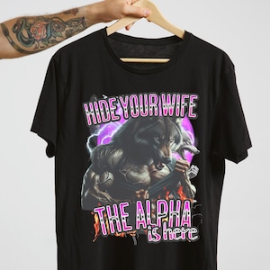 May include: Black t-shirt with a graphic of a wolf with the text "Hide Your Wife The Alpha is Here" in pink.