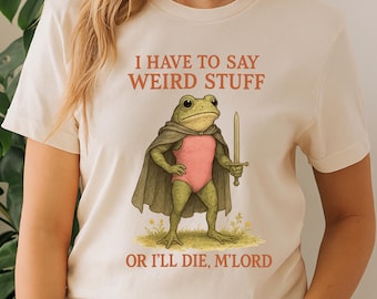 May include: Cream-colored t-shirt featuring a whimsical illustration of a frog dressed as a knight, holding a sword. The frog wears a pink leotard and a green cape. Text on the shirt reads "I HAVE TO SAY WEIRD STUFF OR I'LL DIE, M'LORD."