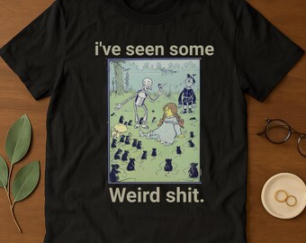 Peut inclure: T-shirt noir avec le texte "i've seen some Weird shit." Le t-shirt présente un graphisme coloré d'un squelette, d'une fille et d'autres personnages dans un champ avec de nombreux rats noirs. Le t-shirt est fait d'une matière douce.