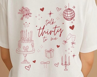 May include: A white t-shirt featuring a red line-art graphic on the back. The design includes a birthday cake, a bouquet, a disco ball, champagne flutes, a gift, and a candelabra, with the text "talk thirty to me" written in the center.