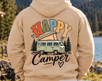 May include: A beige hooded sweatshirt featuring a graphic on the back. The design displays a light green camper van with a pop-up roof, surrounded by pine trees and small hearts. The text "HAPPY" appears in colorful bubble letters above, with "Camper" below.