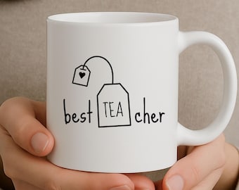 May include: White ceramic mug with a black graphic of a tea bag and the words "best TEA cher". The mug has a large handle and is held by a person.