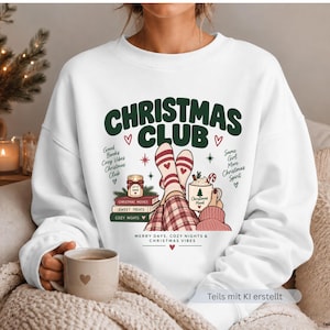 May include: A white long-sleeve sweatshirt featuring a graphic print with the text CHRISTMAS CLUB. The design includes stacked books, a candle, a mug, and legs in patterned socks. Additional text reads Good Books, Cozy Vibes, Christmas Club, Same Girl, More Christmas Spirit, and MERRY DAYS, COZY NIGHTS & CHRISTMAS VIBES.