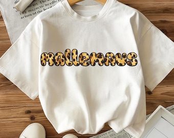 May include: A white t-shirt with the word "mallemaus" in a leopard print design across the chest. The shirt is short-sleeved and appears to be made of a soft material. The shirt is hanging on a wooden hanger.