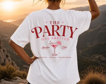 May include: A white t-shirt featuring red and pink graphic text on the back that reads THE PARTY HAS ARRIVED, with an illustration of a cocktail glass, the words Aperitivo Club, and the text APERITIVO DANCING BAD DECISIONS at the bottom.
