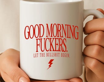 May include: A white ceramic mug featuring red text that reads GOOD MORNING FUCKERS. LET THE BULLSHIT BEGIN. with a small red lightning bolt icon centered below the text. The mug has a standard handle and a smooth, cylindrical body design.