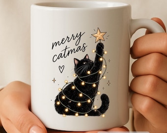 May include: A white ceramic mug featuring a black cat wrapped in glowing string lights, reaching up to place a gold star on top. The text merry catmas is printed in black script above the cat, accompanied by a small heart and star icons.