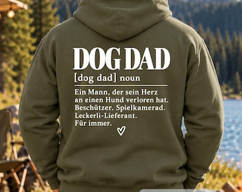 May include: An olive green hooded sweatshirt featuring white text on the back that reads DOG DAD [dog dad] noun, followed by a German definition of a dog dad, and a small white heart symbol centered at the bottom of the printed text block.