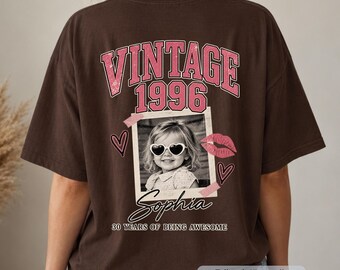 May include: A dark brown t-shirt featuring a back graphic with the text VINTAGE 1996, a photo of a child wearing heart-shaped sunglasses, the name Sophia, and the text 30 YEARS OF BEING AWESOME, accented with pink hearts and a lip print.
