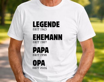 May include: White t-shirt with black text. The text reads "LEGENDE Seit 1963", "EHEMANN Seit 1987", "PAPA Seit 1998", and "OPA Seit 2026". The shirt is being worn by a person.